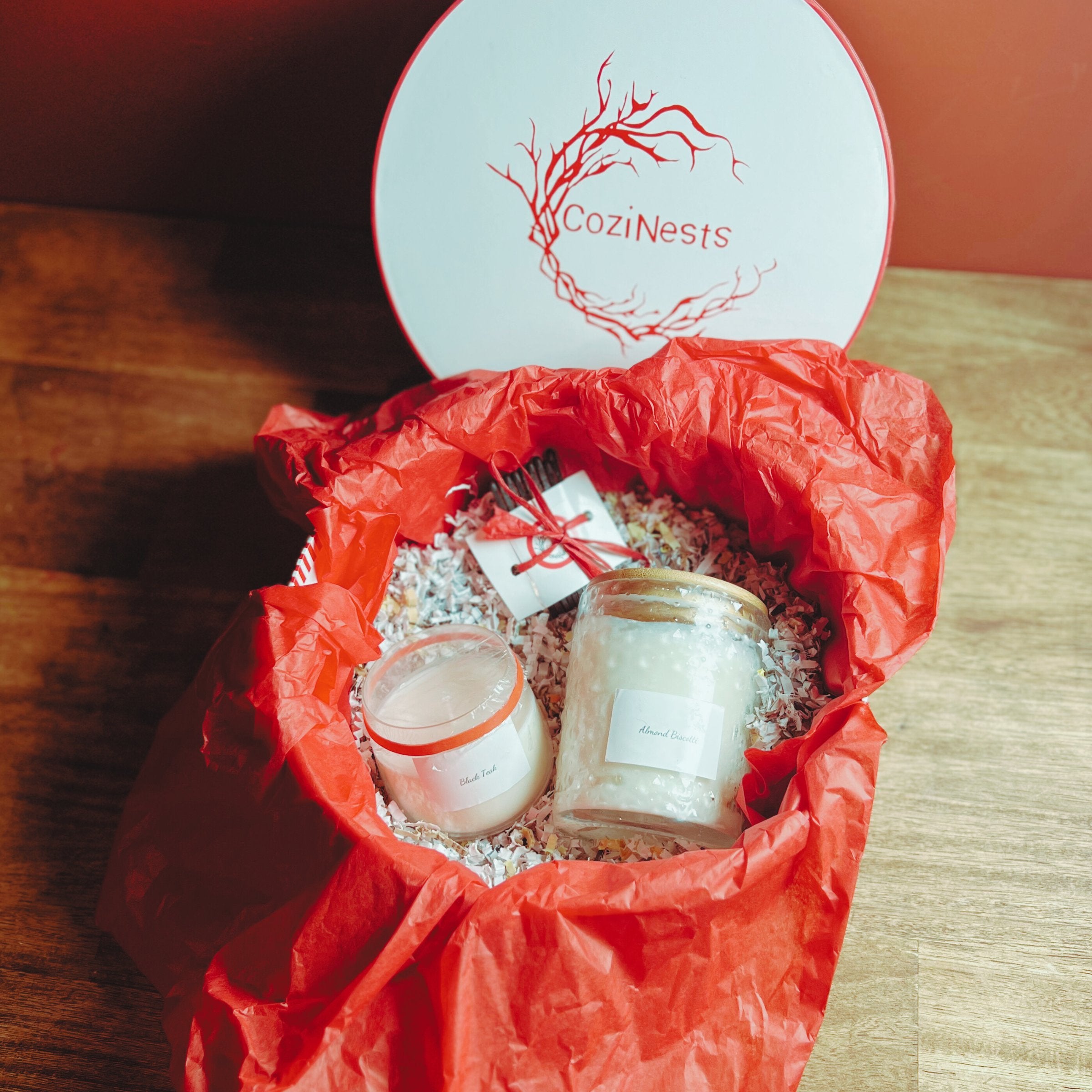 gift box, red tissue paper, two candles, matches, coziNests logo on the top off round box